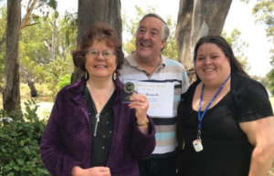 three people holding a certificate in front of trees